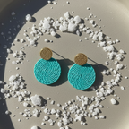 Turquoise earrings with gold accents on a textured surface with small stones.