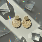 Pair of round gold earrings on a reflective surface with geometric shapes and rainbow