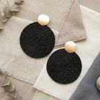 Black woven coasters with gold accents on a textured surface with eucalyptus leaves.