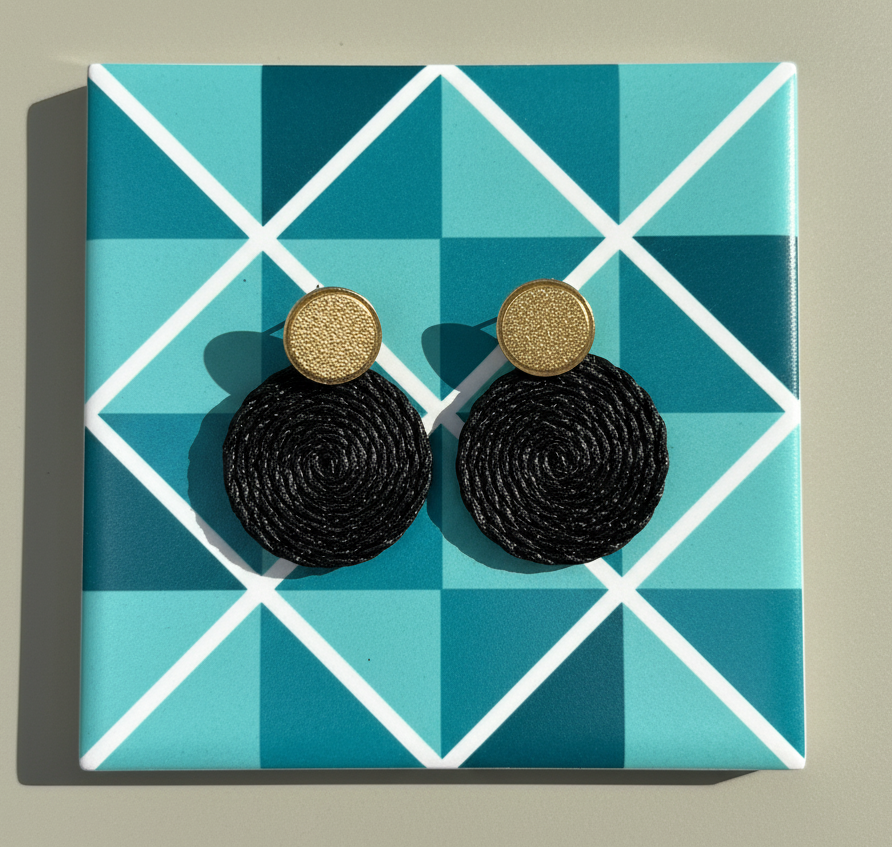 Black earrings with gold accents on a blue geometric patterned card