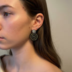Close-up of a person wearing a black Manila earring with a neutral background