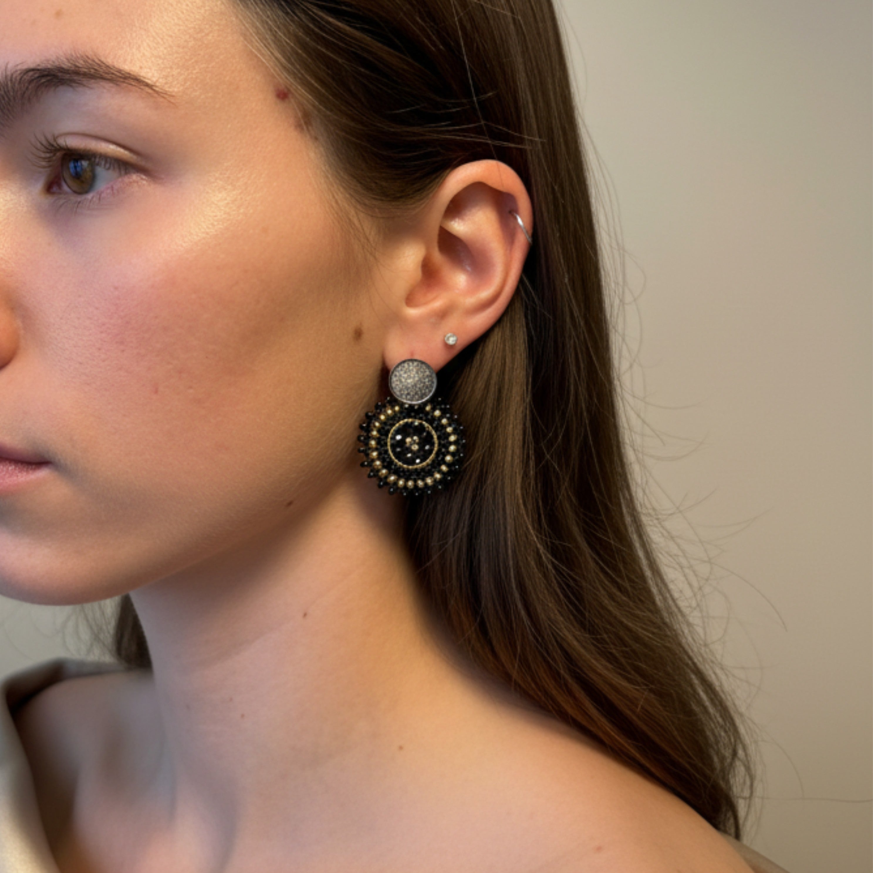 Close-up of a person wearing a black Manila earring with a neutral background