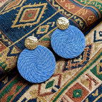 Blue earrings with gold tops on a patterned fabric background