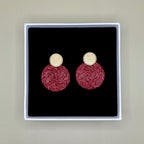 Pair of burgundy earrings in a black box with gold tops and red bases