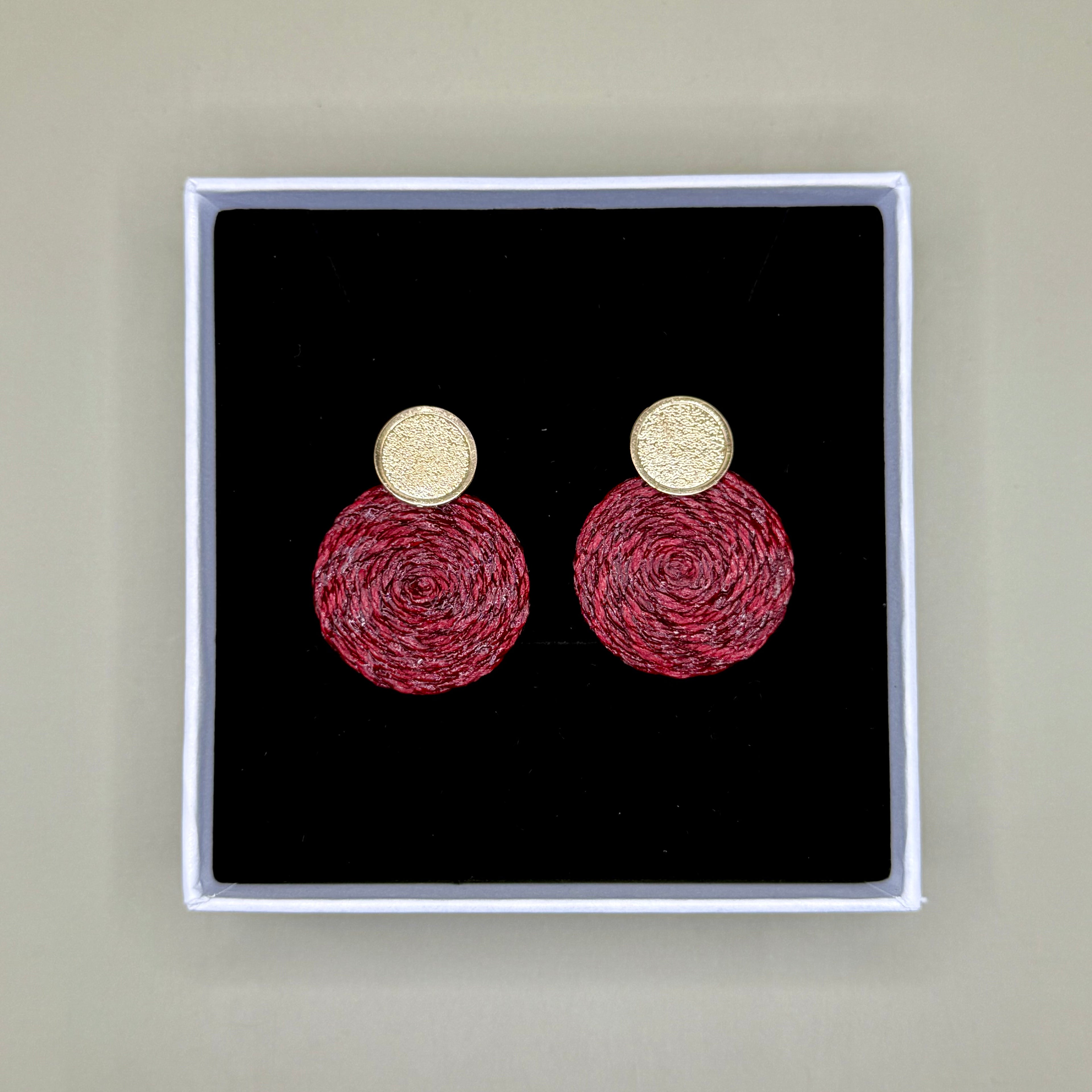 Pair of burgundy earrings in a black box with gold tops and red bases