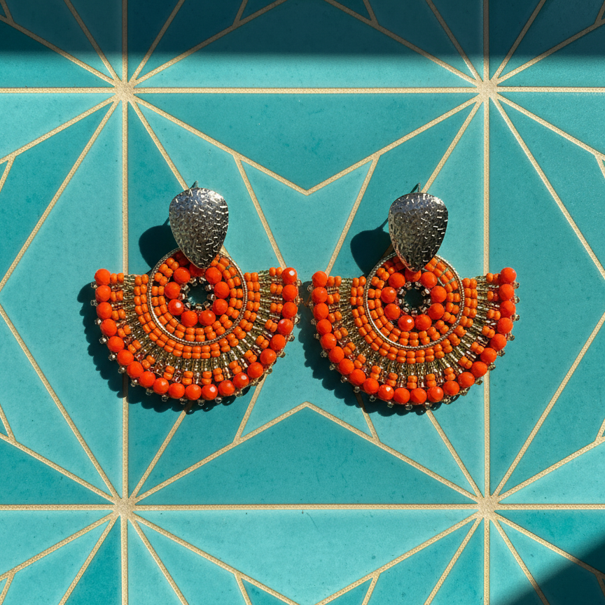 Orange beaded earrings on a teal geometric patterned background