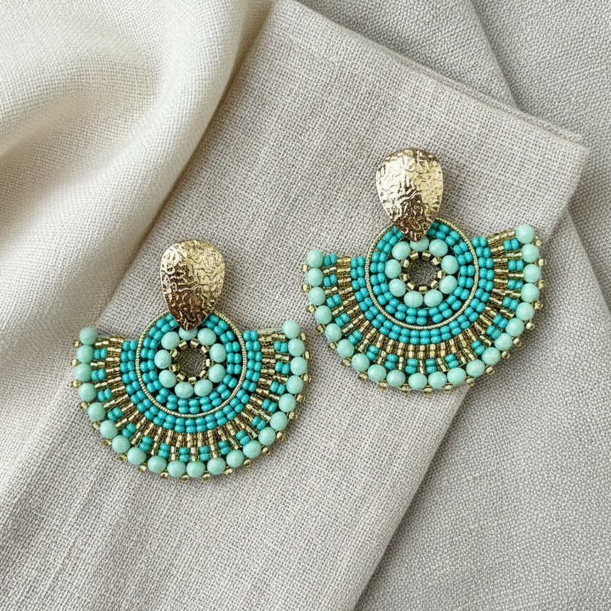 Turquoise beaded earrings with gold accents on a textured fabric background