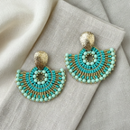 Turquoise beaded earrings with gold accents on a textured fabric background