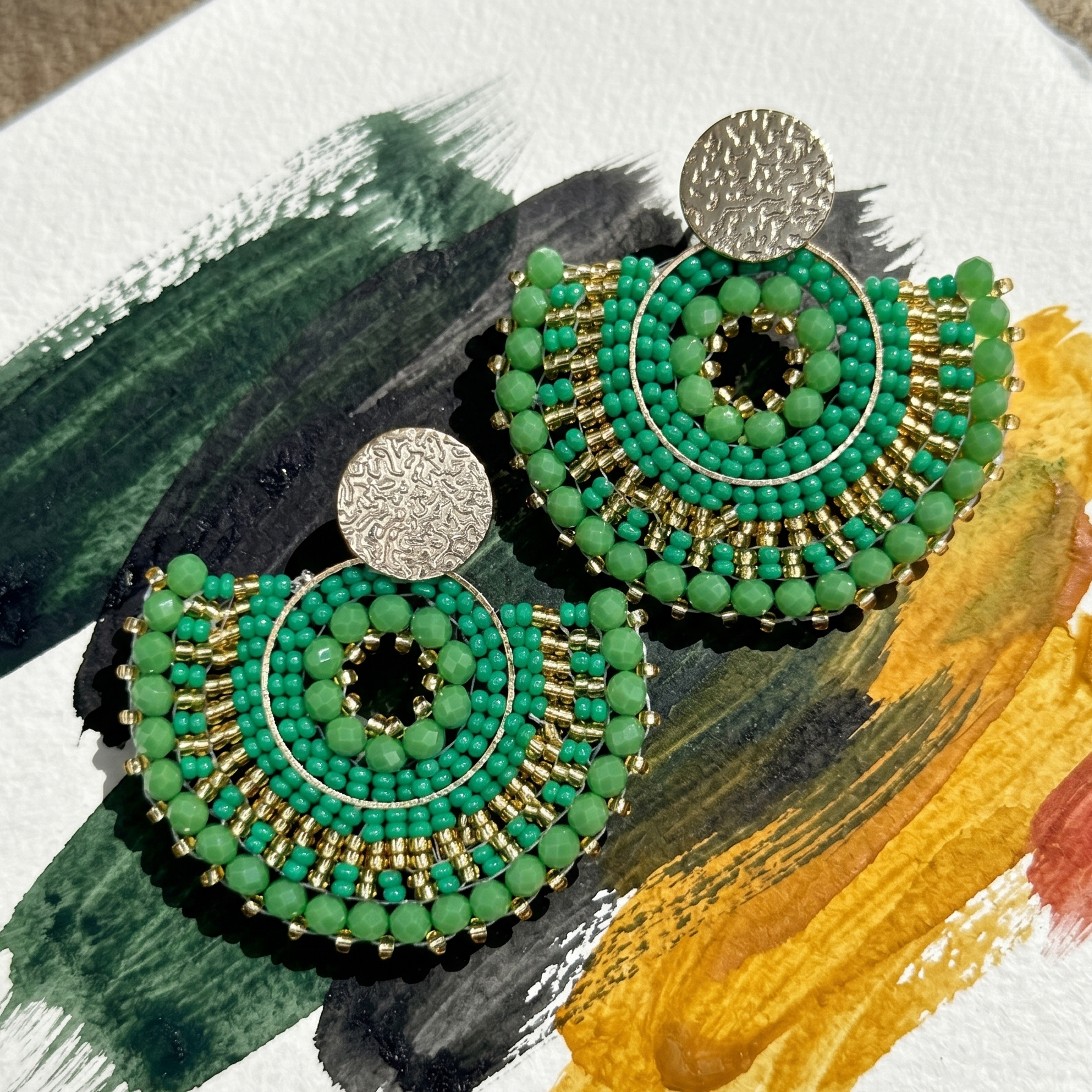 Green beaded earrings on a colorful abstract background