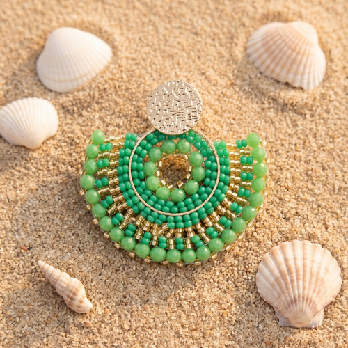 Green beaded earring on sand with shells