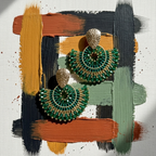 Green and gold earrings on a colorful abstract background