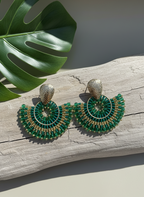 Green beaded earrings on a wooden surface with a leaf in the background