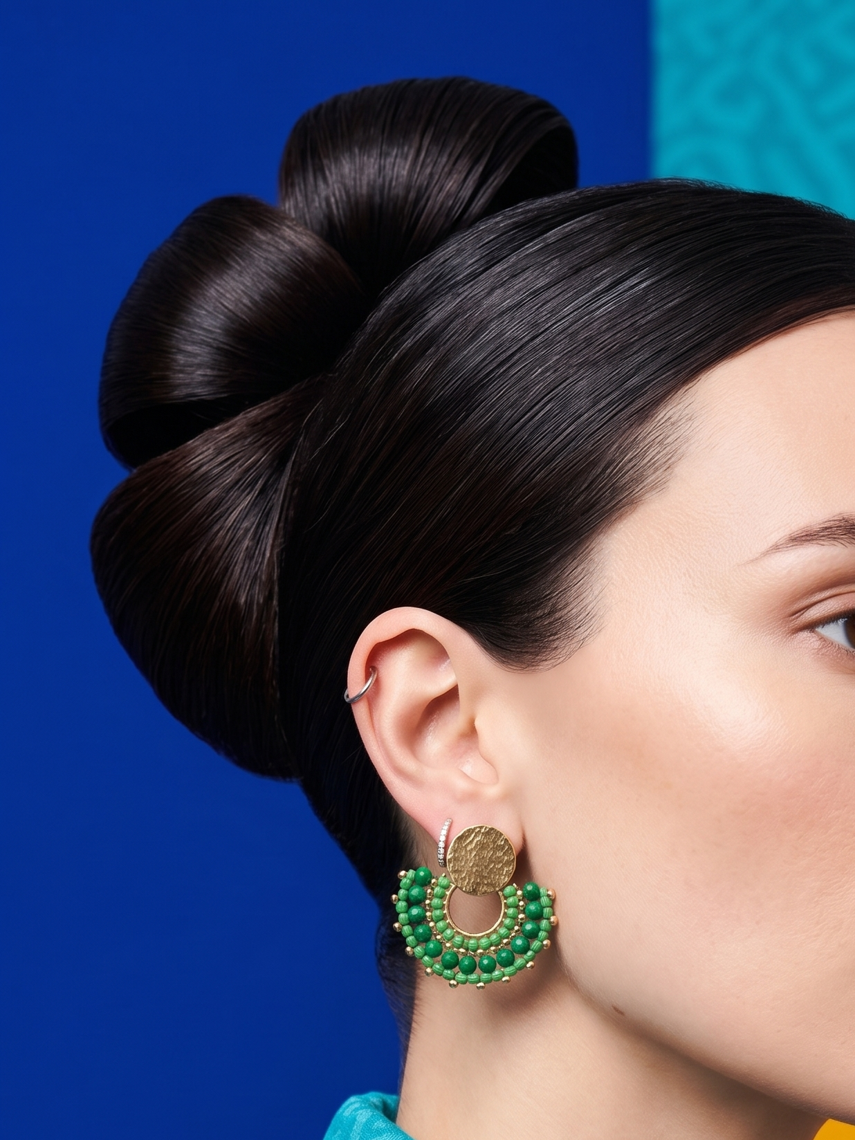 Woman with styled hair and green earrings against a colorful geometric background
