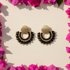 Gold and black earrings on a beige background with pink flowers around