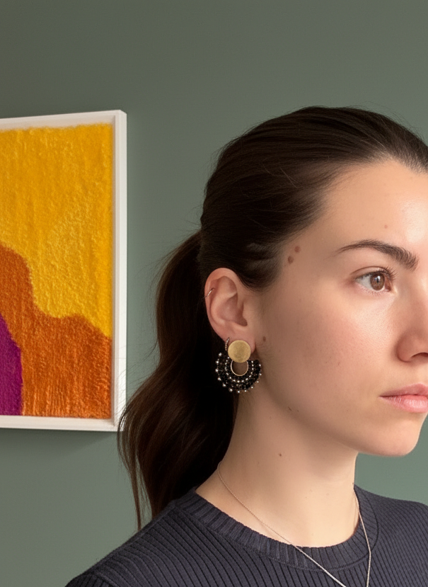 Woman with a ponytail wearing earrings and a necklace, with a colorful abstract painting in the background.