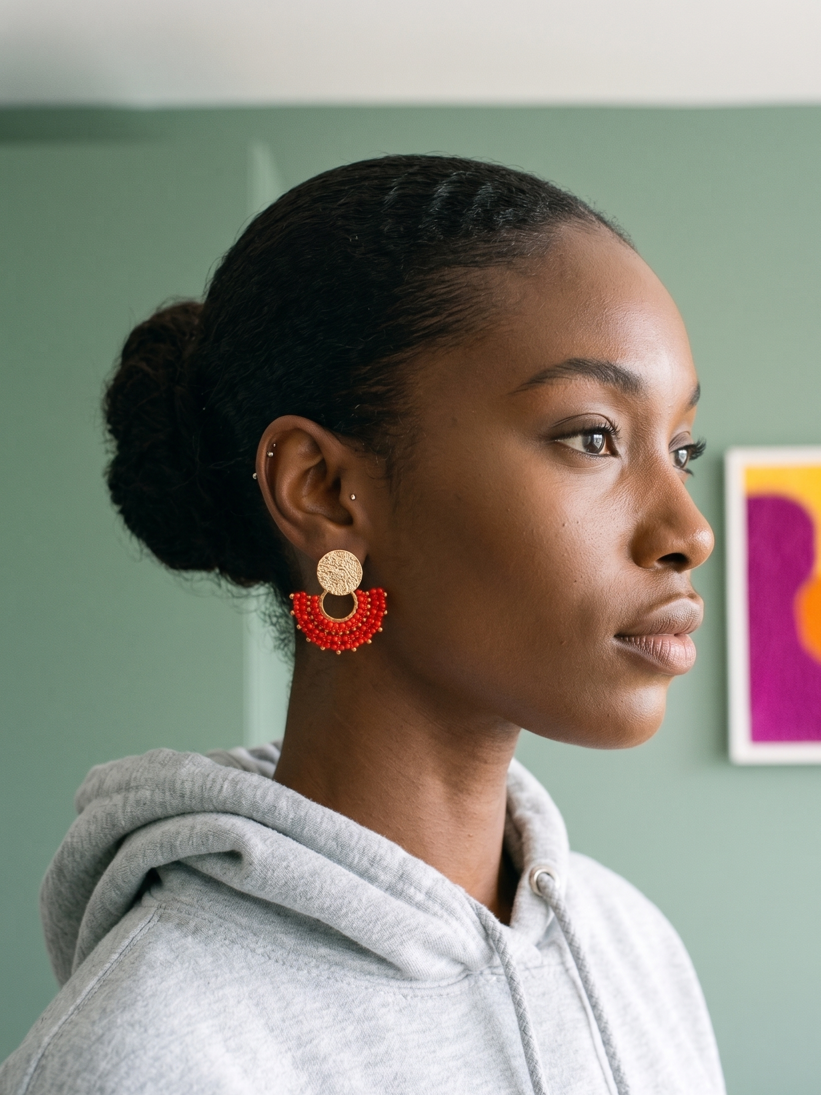 Woman wearing red earrings with a gray hoodie against a light green wall.