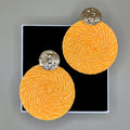 Pair of orange circular earrings with golden tops on a black card against a gray background