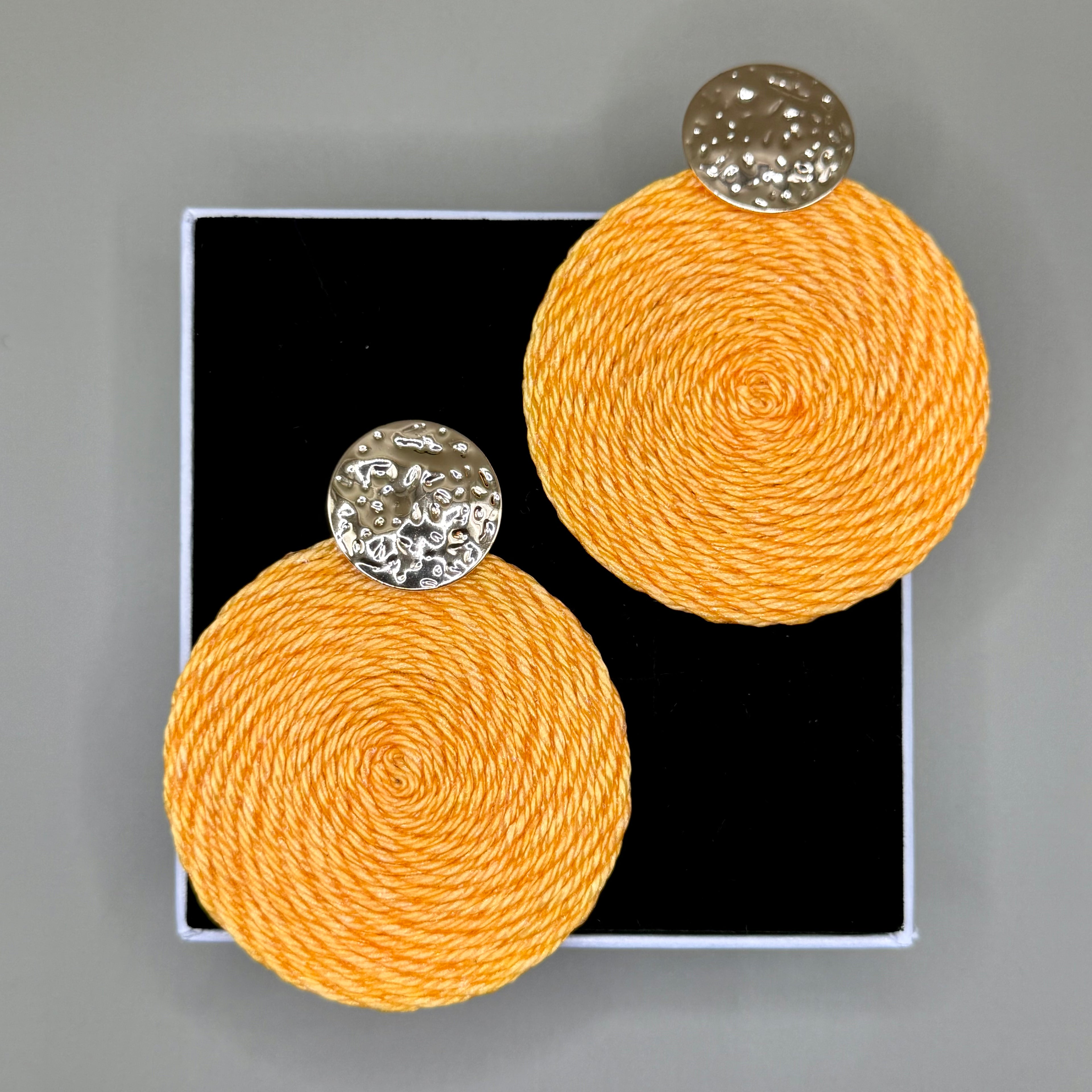 Pair of orange circular earrings with golden tops on a black card against a gray background