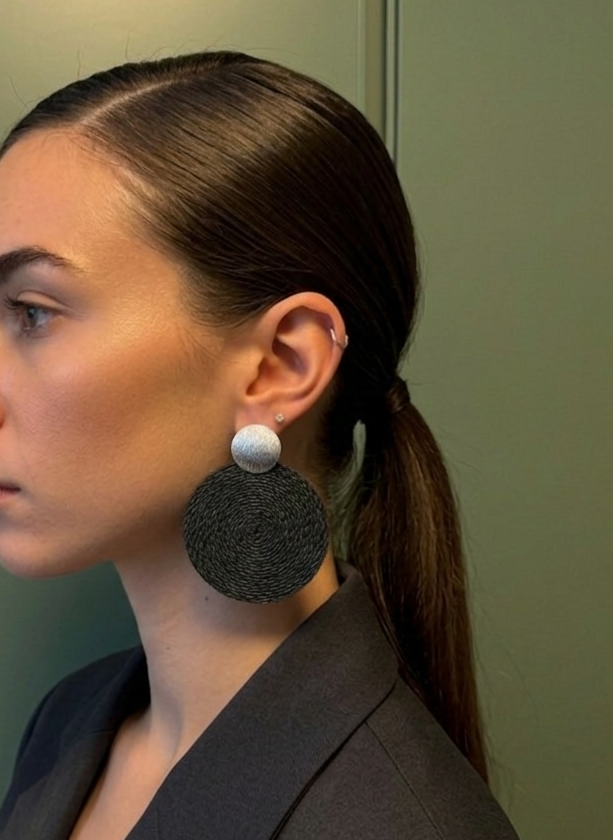 Woman wearing large black earrings against a green wall