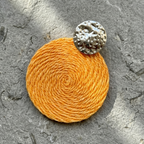 Orange earring with a textured silver top on a gray surface