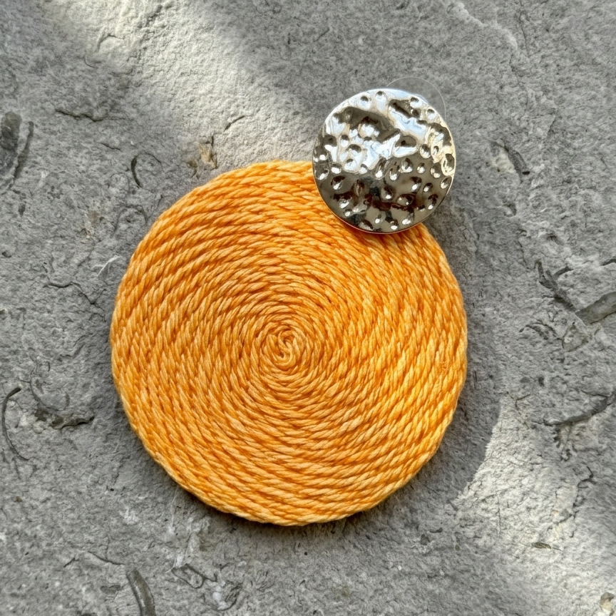 Orange earring with a textured silver top on a gray surface