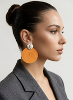 Woman wearing large orange earrings with a gray blazer on a light background