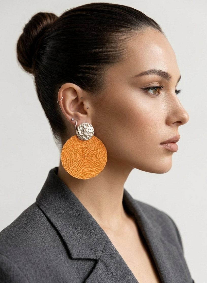 Woman wearing large orange earrings with a gray blazer on a light background