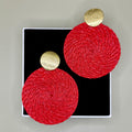 Red circular earrings with gold accents on a black box against a gray background