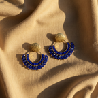Blue earrings with a golden stud on a linen tablecloth