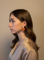 Woman wearing orange earrings against a plain background