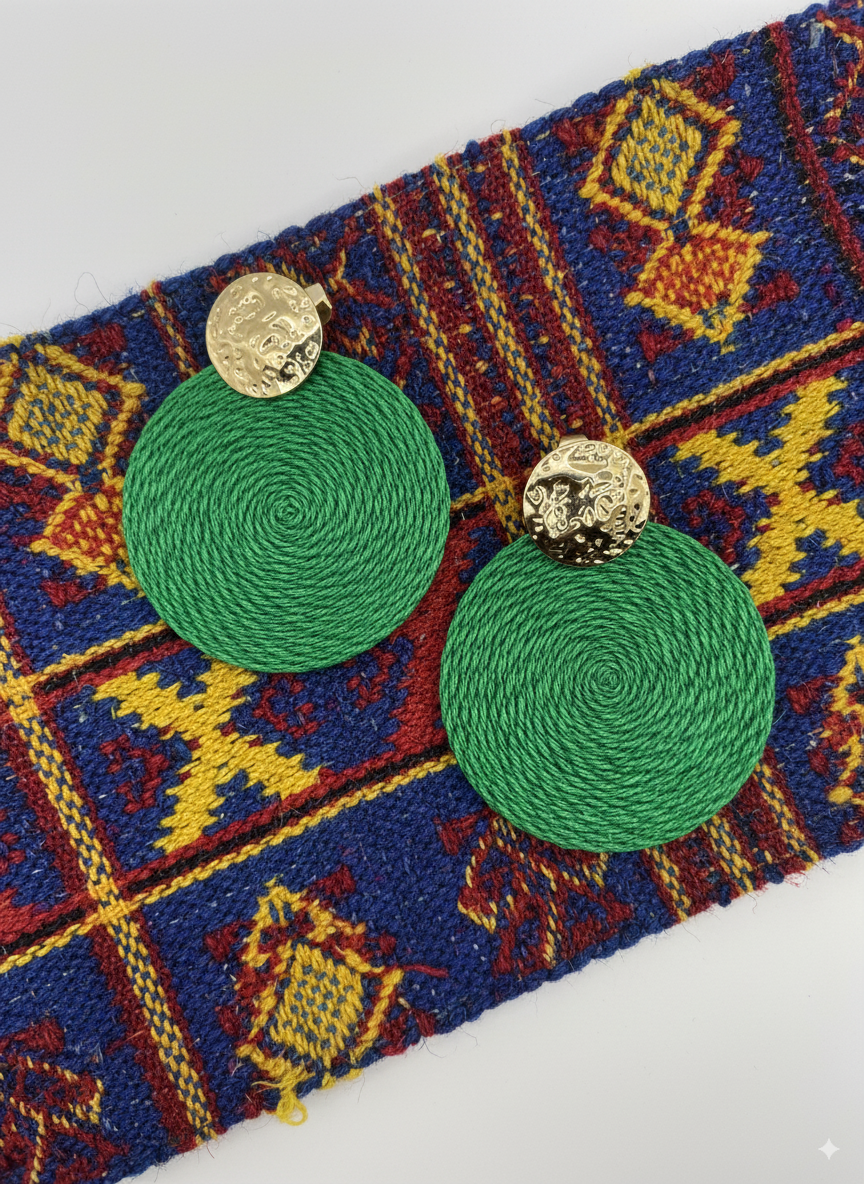 Green earrings with gold tops on a colorful patterned fabric background