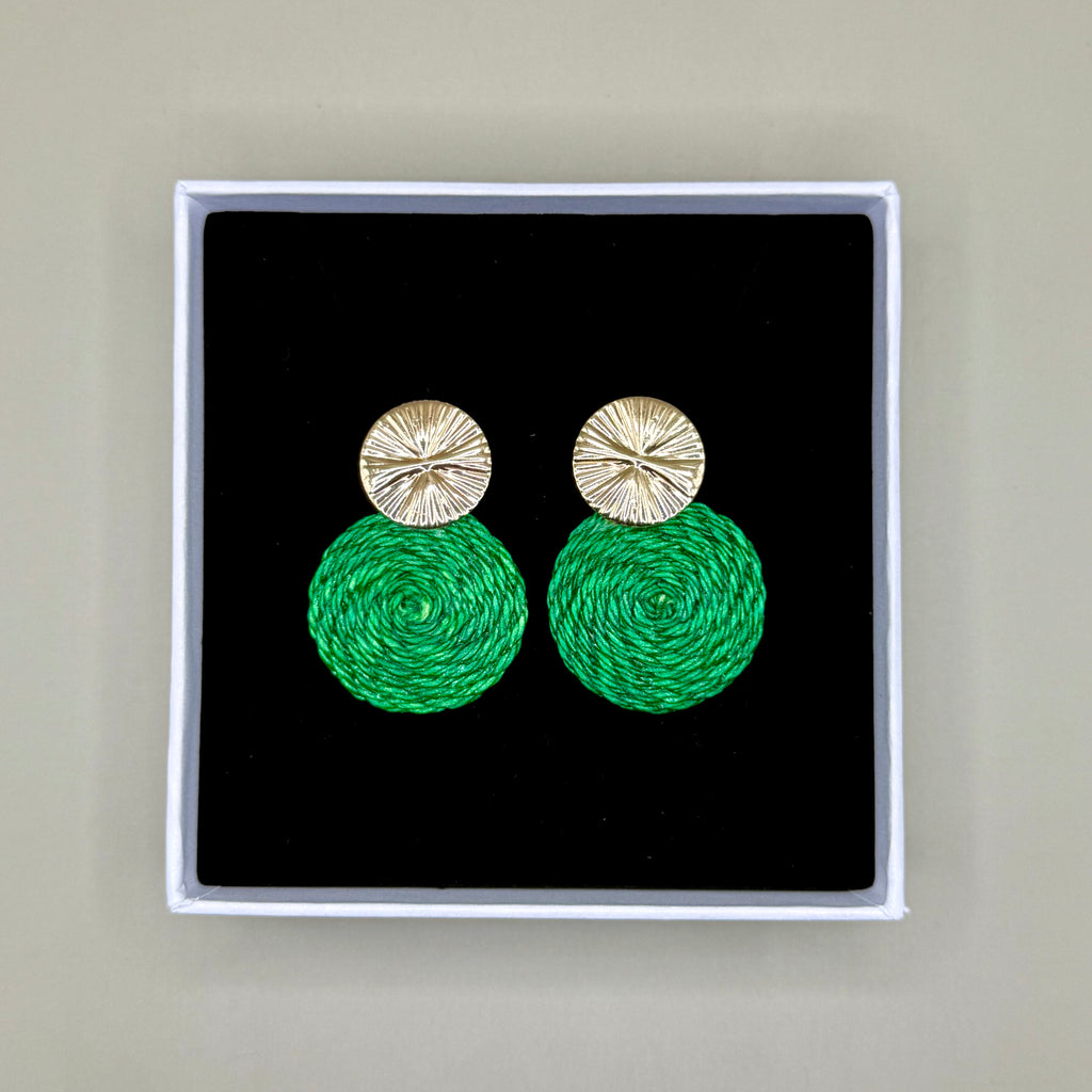 Green earrings with gold tops in a black box on a beige background