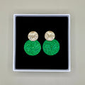 Green earrings with gold tops in a black box on a beige background