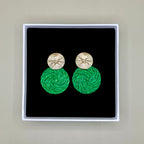Green earrings with gold tops in a black box on a beige background