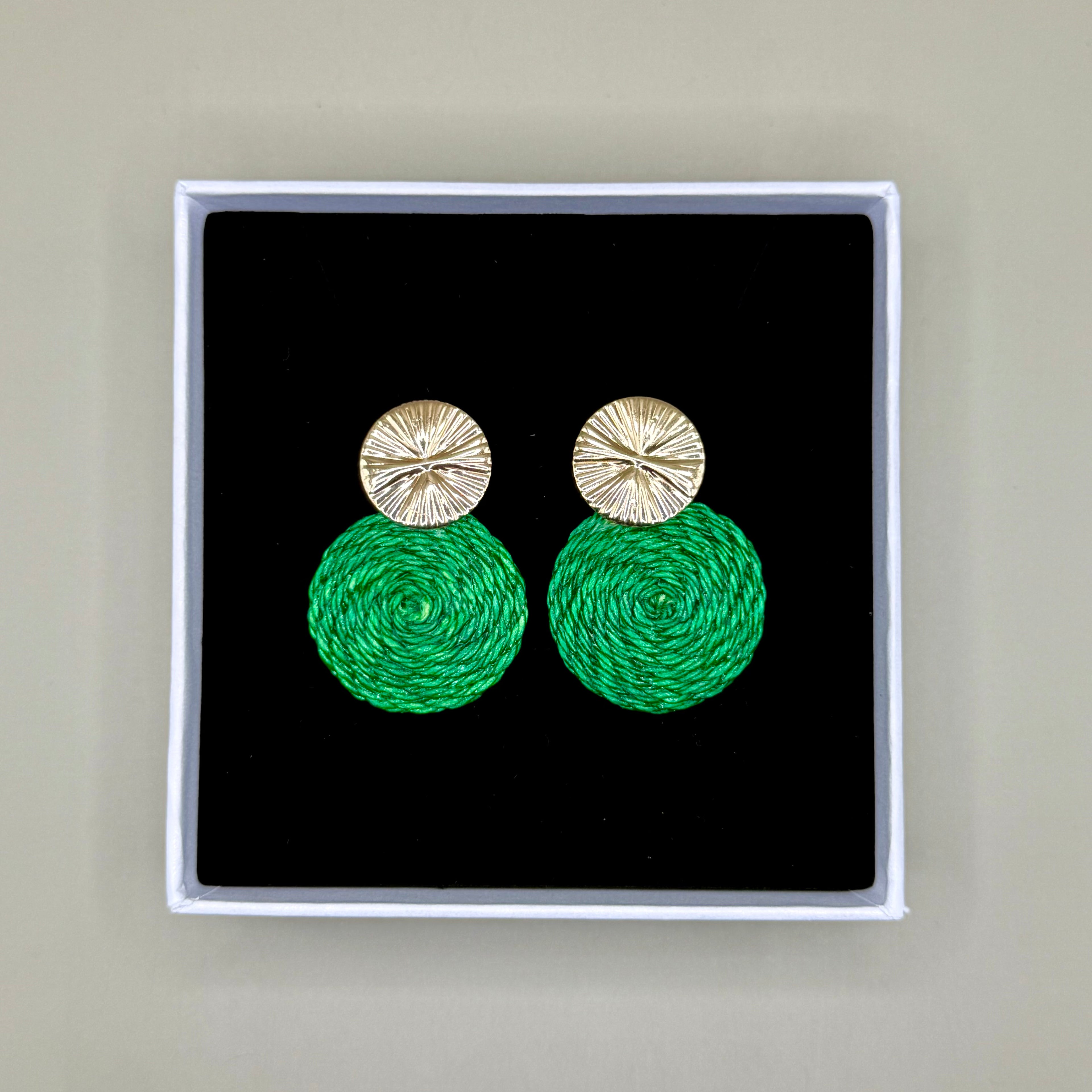 Green earrings with gold tops in a black box on a beige background