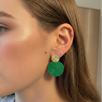 Close-up of a person wearing green earrings with gold accents.