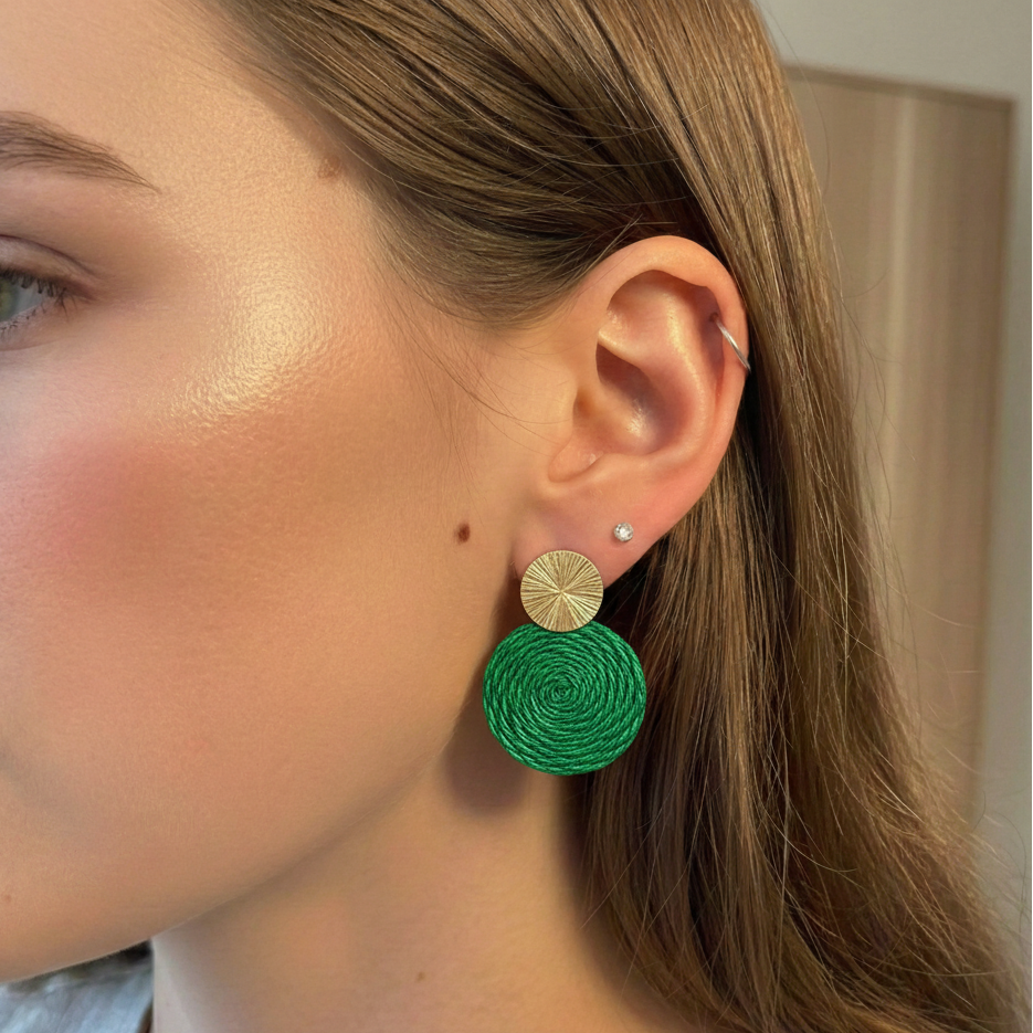Close-up of a person wearing green earrings with gold accents.