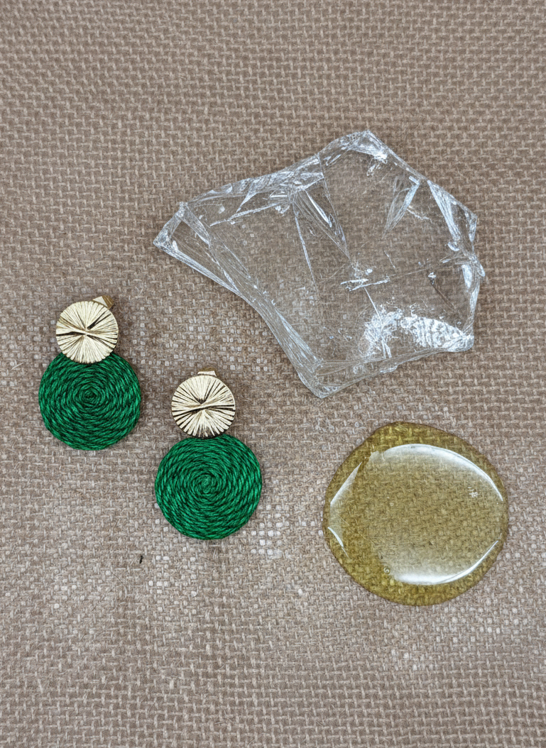 Green and gold earrings on a textured surface with clear plastic packaging.