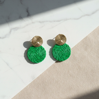 Green round earrings with gold tops on a marble surface