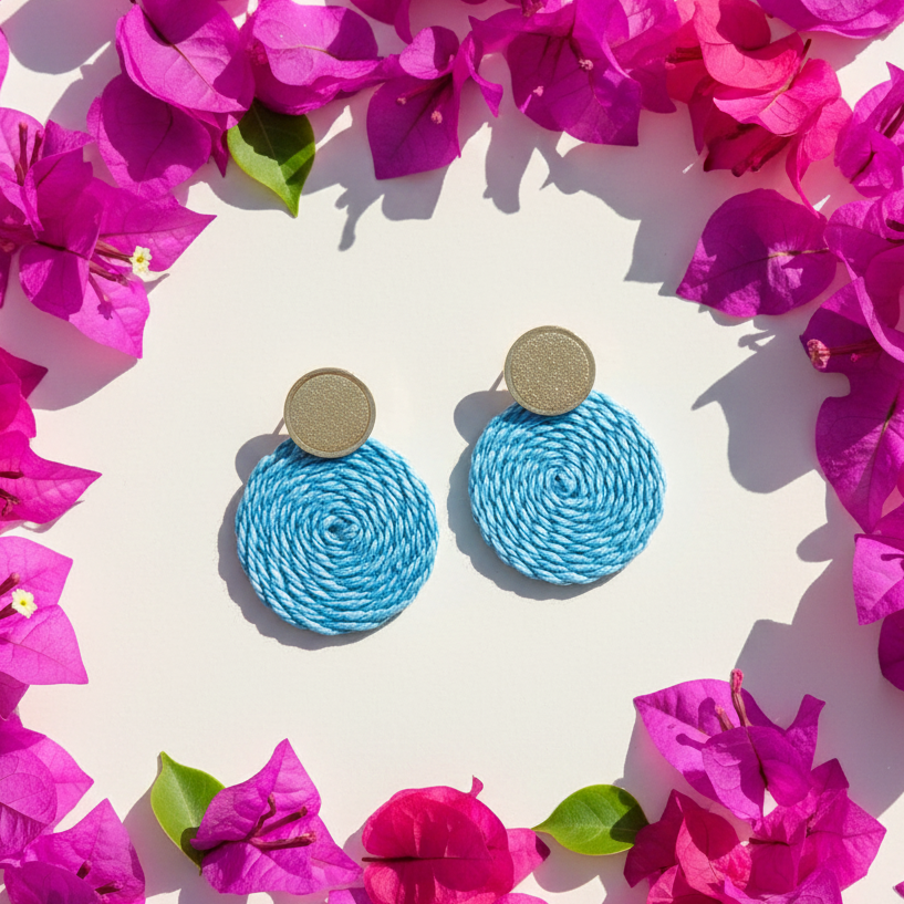Blue circular earrings surrounded by pink flowers on a white background