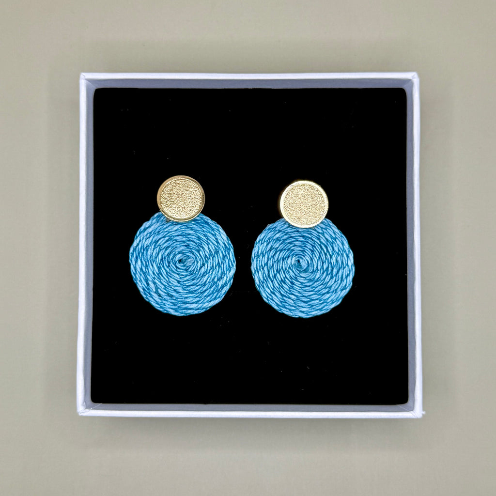 Light blue earrings with gold tops in a black box on a beige background