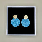 Light blue earrings with gold tops in a black box on a beige background