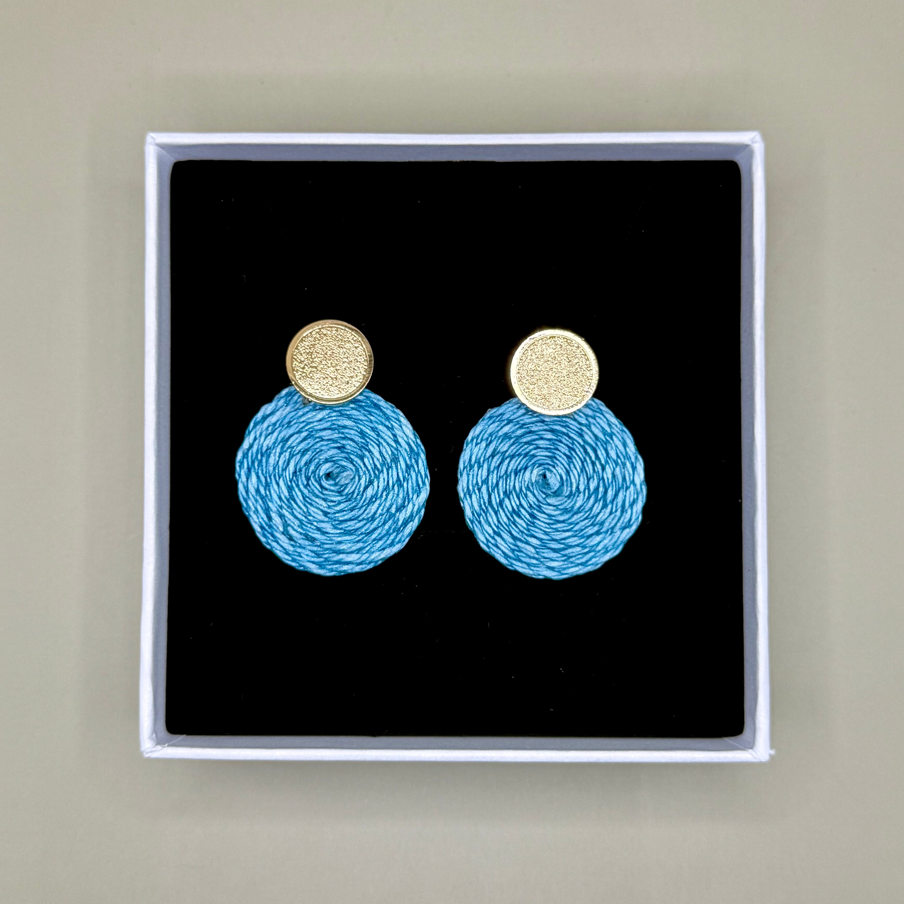 Light blue earrings with gold tops in a black box on a beige background