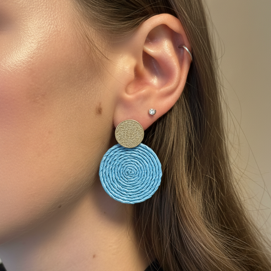 Close-up of a person wearing blue and gold earrings with a neutral background