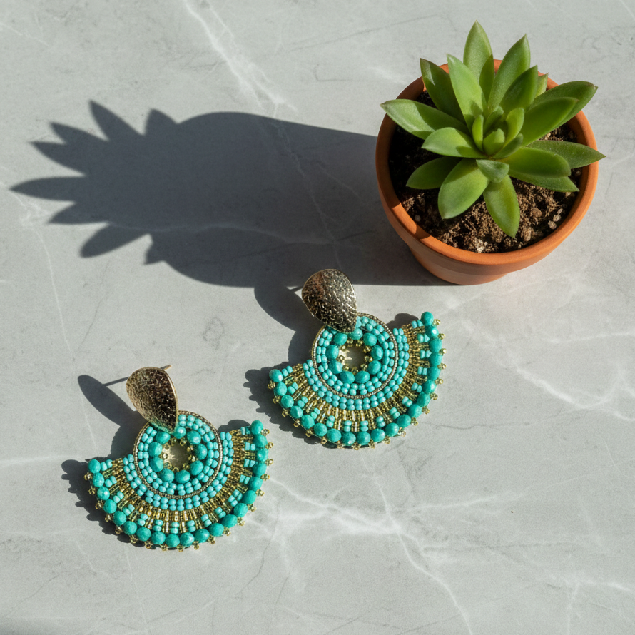 Light Blue beaded earrings on a textured surface with a potted plant.