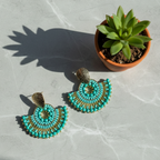 Light Blue beaded earrings on a textured surface with a potted plant.