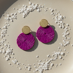 Magenta circular earrings with gold posts on a beige plate with decorative stones.