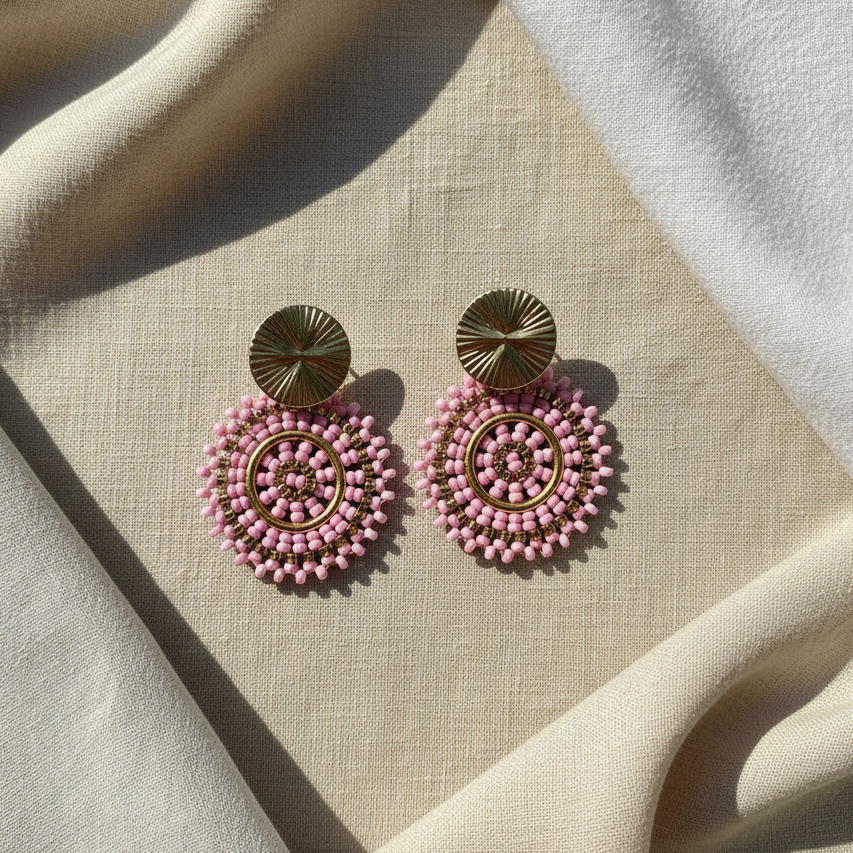 Pink beaded earrings with gold accents on a beige fabric background