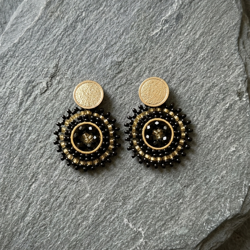 Pair of black and gold beaded earrings on a gray stone surface