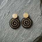 Pair of black and gold beaded earrings on a gray stone surface